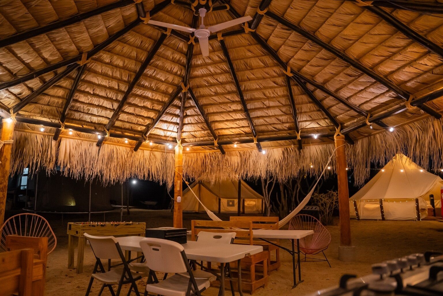 Illuminated tents and relaxed outdoor seating beneath the palapa