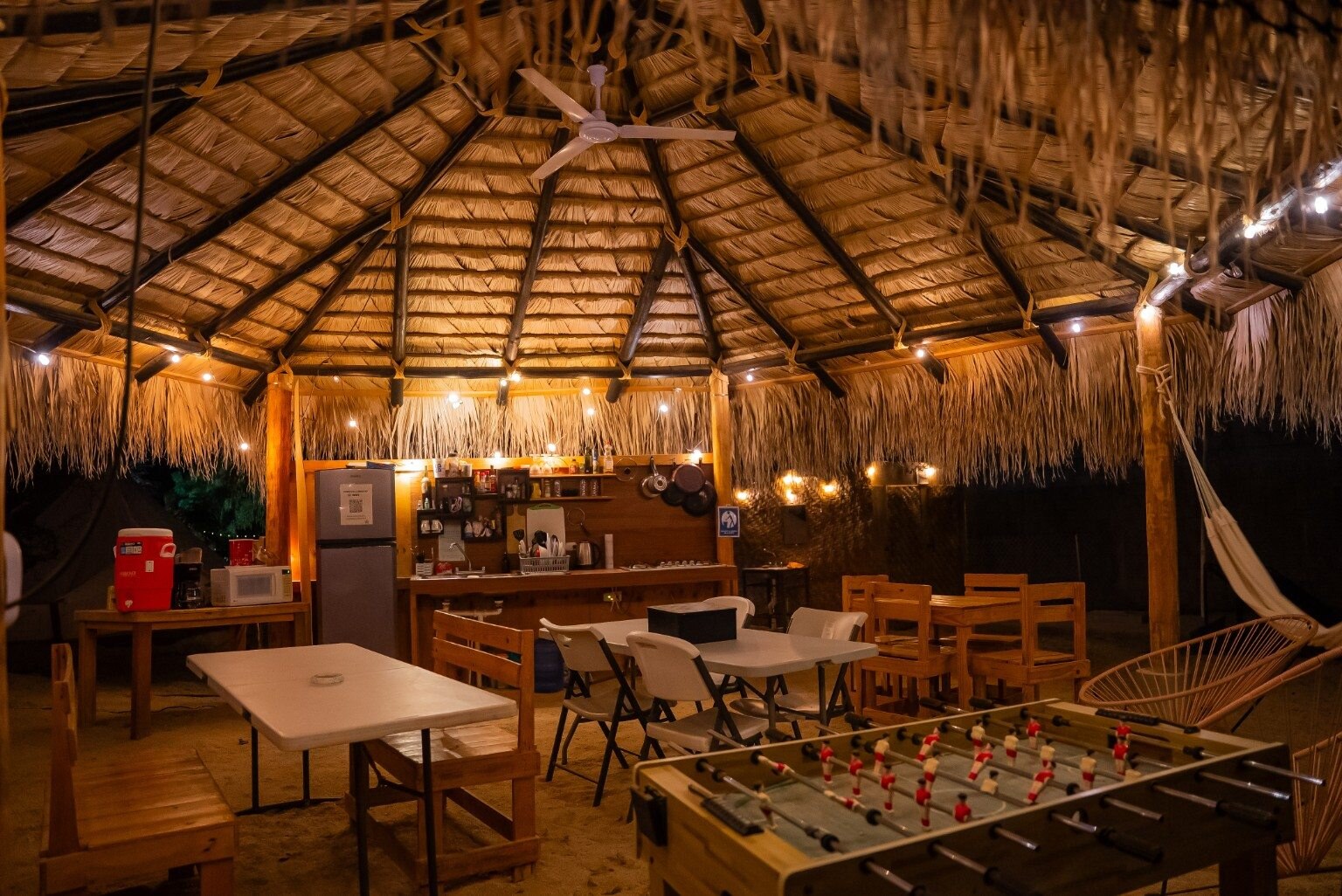 Warmly lit shared palapa with tables and kitchen
